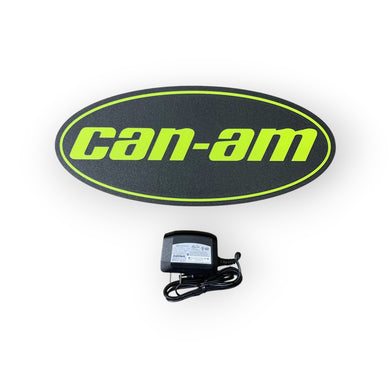 Can-Am led indoor sign on a black oval with a power adapter below on a white background